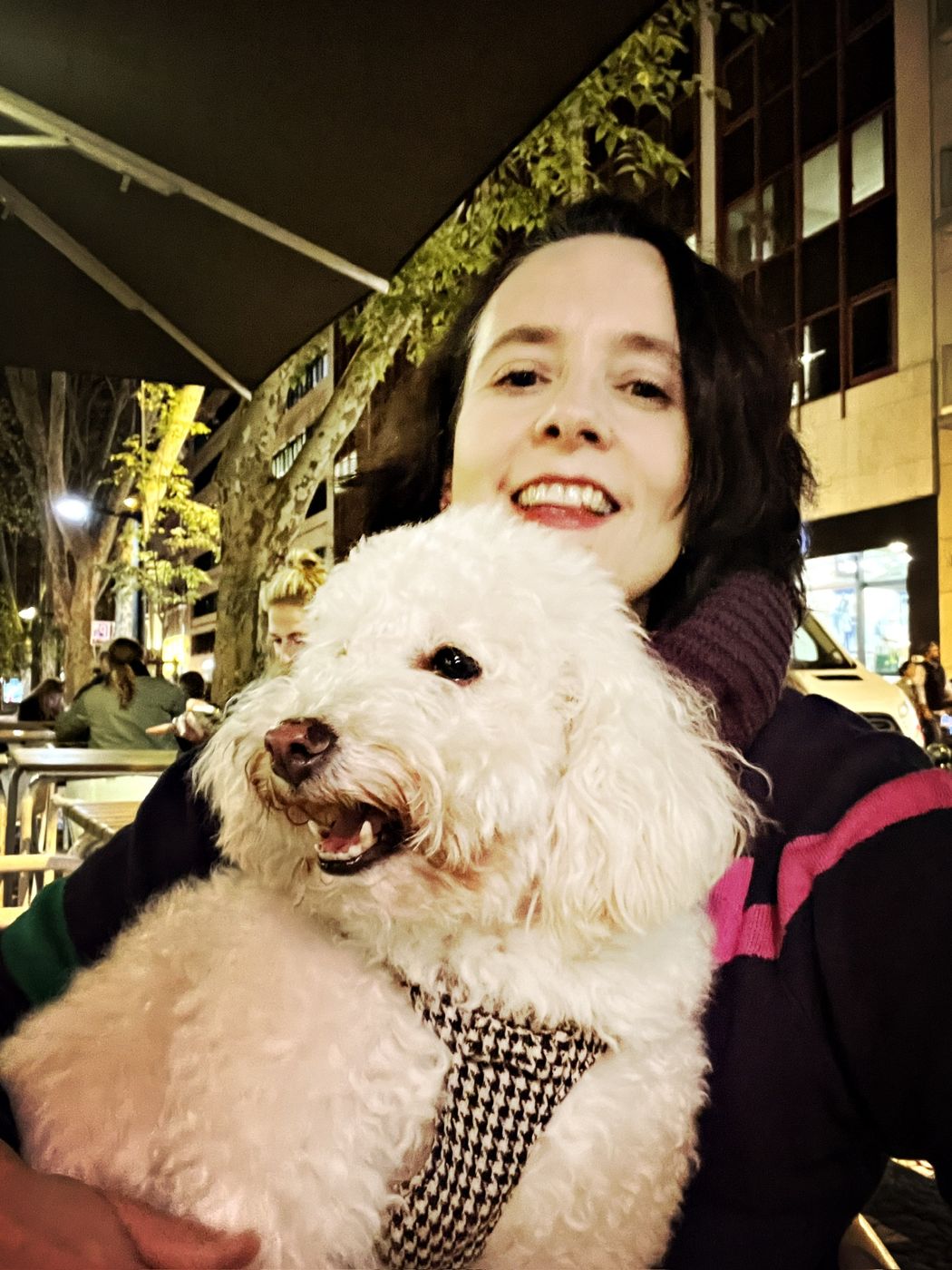Hilary smiling at a cafe terrace at night, holding a fluffy white poodle